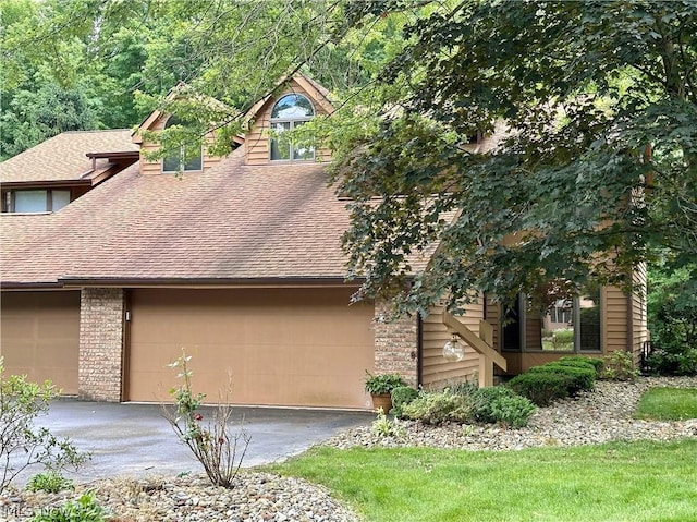 view of home's exterior with brick siding, an attached garage, roof with shingles, and driveway