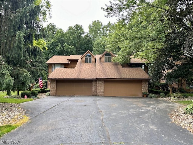 view of front facade with aphalt driveway, brick siding, roof with shingles, and a garage