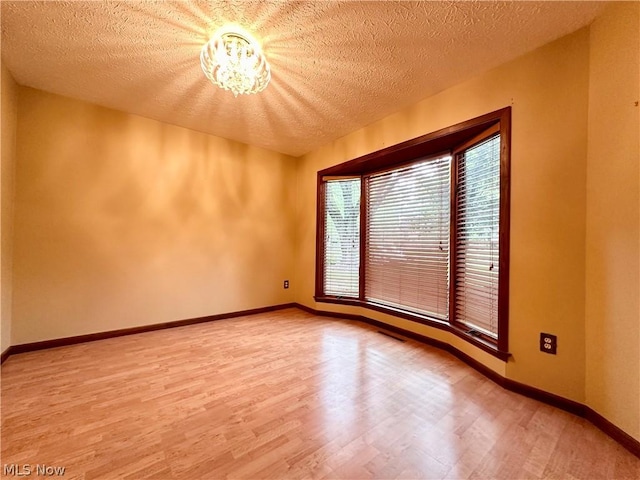 unfurnished room featuring visible vents, light wood-style flooring, a textured ceiling, an inviting chandelier, and baseboards