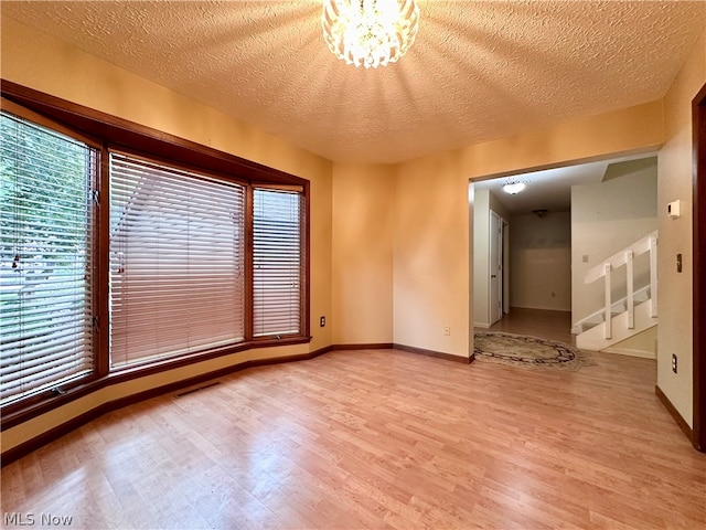 unfurnished room featuring light hardwood / wood-style floors, a textured ceiling, and a chandelier