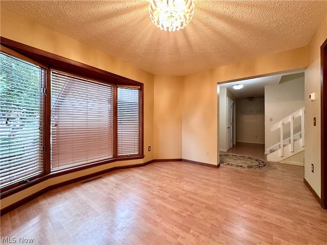 spare room featuring an inviting chandelier, baseboards, light wood-type flooring, and a textured ceiling