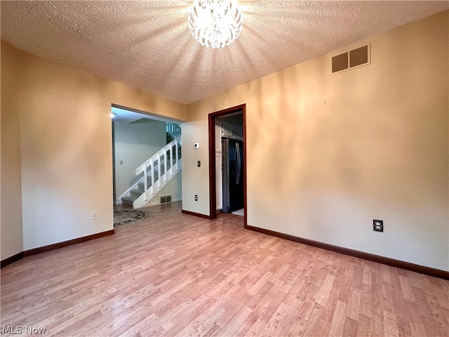 unfurnished room featuring wood-type flooring, an inviting chandelier, and a textured ceiling