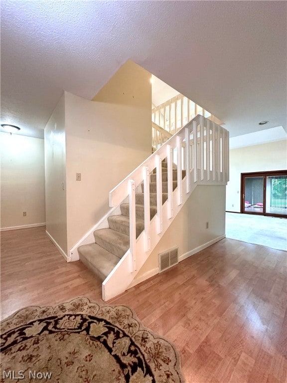 stairs with a textured ceiling and wood-type flooring