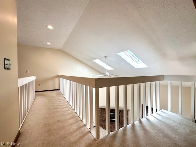 corridor with light carpet, a textured ceiling, and lofted ceiling with skylight