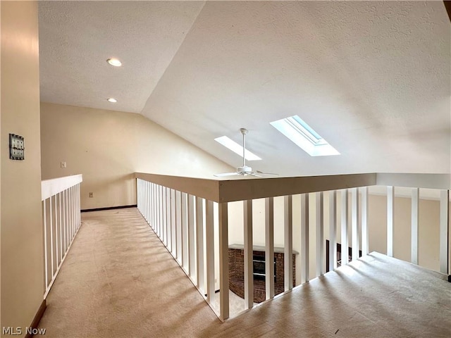 corridor with baseboards, vaulted ceiling with skylight, recessed lighting, a textured ceiling, and light carpet