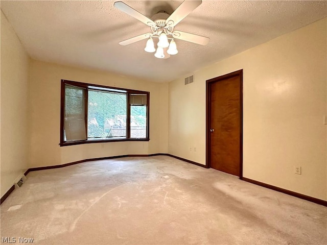 empty room with light carpet, visible vents, a textured ceiling, and baseboards