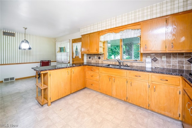 kitchen featuring decorative light fixtures, kitchen peninsula, sink, and dark stone counters