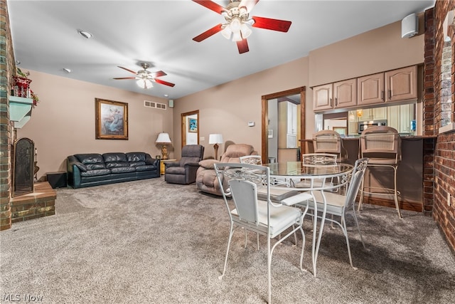 dining area featuring brick wall, carpet, a brick fireplace, and ceiling fan