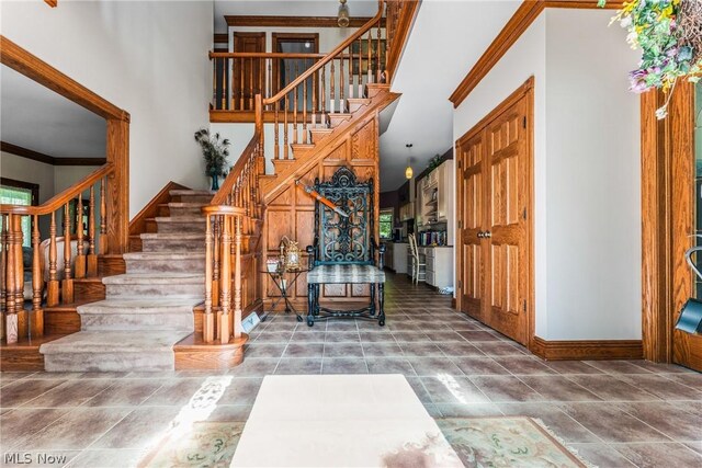 staircase with a towering ceiling, tile flooring, and crown molding