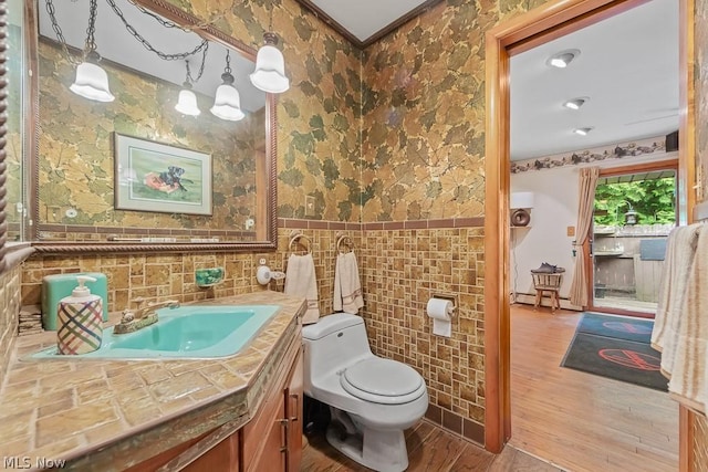 half bathroom with toilet, a baseboard heating unit, wood finished floors, vanity, and tile walls