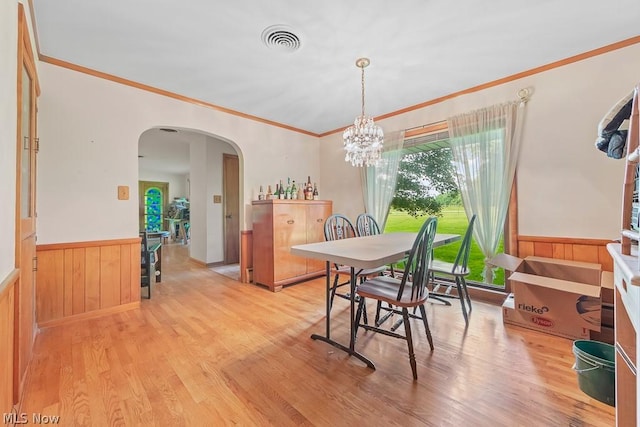 dining room with arched walkways, light wood-style flooring, wainscoting, and visible vents