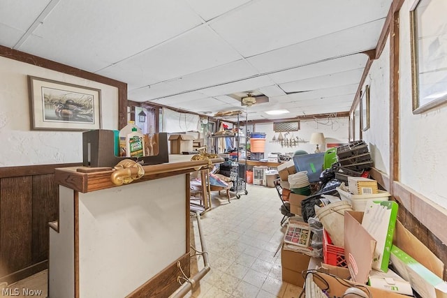 misc room featuring light floors, a drop ceiling, wainscoting, and wooden walls