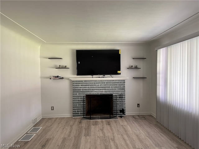 unfurnished living room with plenty of natural light, light wood-type flooring, and a brick fireplace