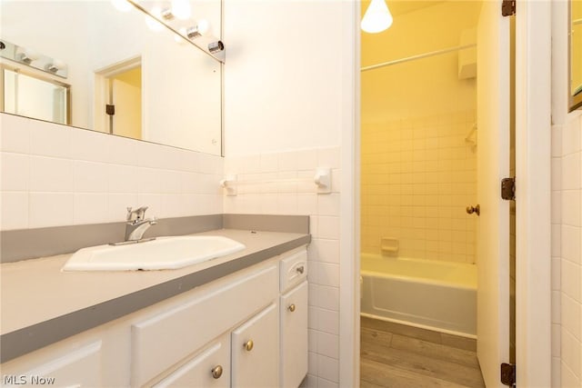 bathroom featuring hardwood / wood-style floors, vanity, tiled shower / bath, tile walls, and tasteful backsplash