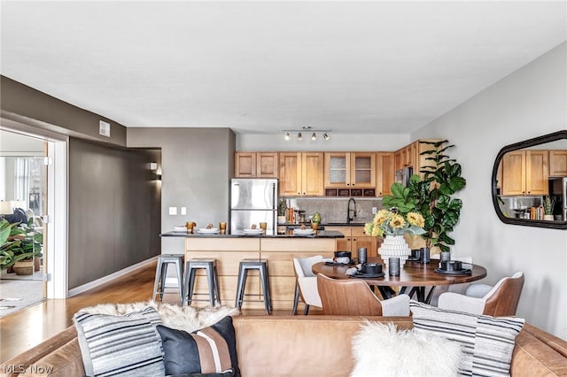 kitchen with a kitchen bar, stainless steel fridge, tasteful backsplash, sink, and light hardwood / wood-style floors