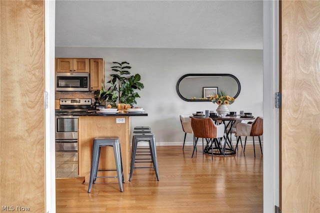 kitchen with a kitchen bar, backsplash, stainless steel appliances, and light hardwood / wood-style floors