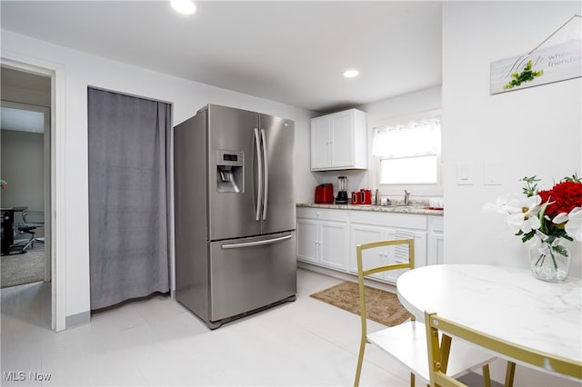 kitchen with light stone countertops, stainless steel refrigerator with ice dispenser, white cabinetry, and sink