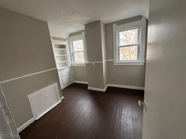 unfurnished room featuring built in shelves, a healthy amount of sunlight, and dark hardwood / wood-style flooring