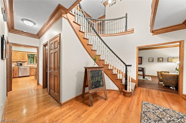 stairway with wood-type flooring, ornamental molding, and a textured ceiling