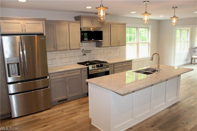 kitchen featuring light hardwood / wood-style floors, appliances with stainless steel finishes, a kitchen island with sink, sink, and tasteful backsplash