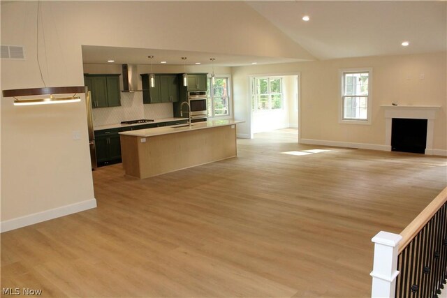 kitchen with light hardwood / wood-style floors, a kitchen island with sink, backsplash, and green cabinetry