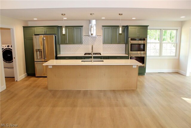 kitchen with stainless steel appliances, wall chimney range hood, a kitchen island with sink, and green cabinets