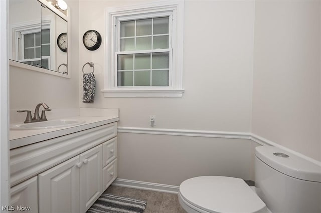 half bathroom featuring baseboards, toilet, and vanity