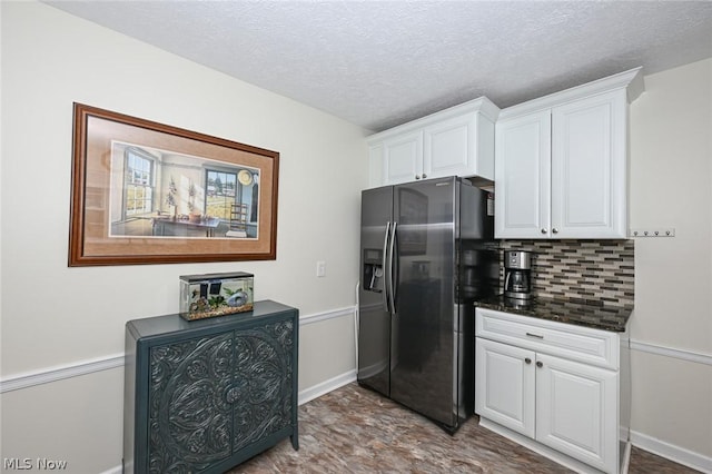 kitchen with dark countertops, refrigerator with ice dispenser, decorative backsplash, white cabinets, and a textured ceiling