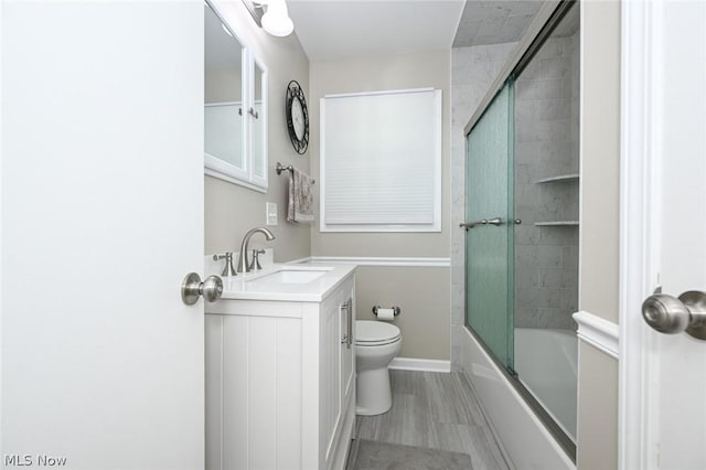 full bath with vanity, wood finished floors, baseboards, shower / bath combination with glass door, and toilet