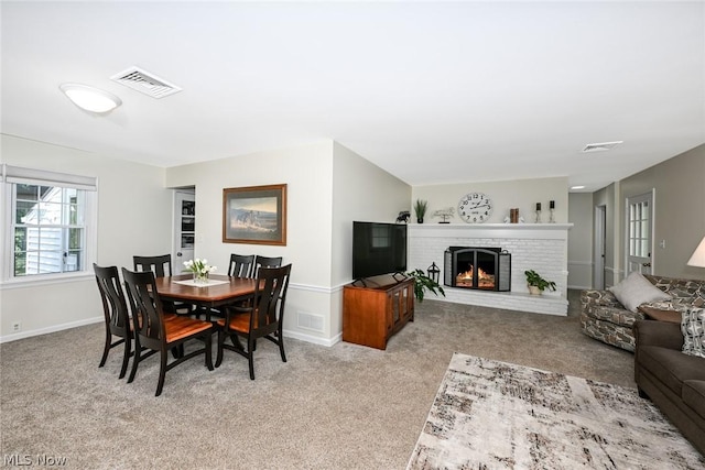 dining area featuring visible vents, light colored carpet, a brick fireplace, and baseboards