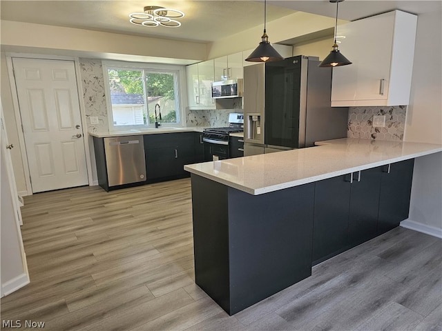 kitchen with white cabinets, stainless steel appliances, decorative light fixtures, and light wood-type flooring