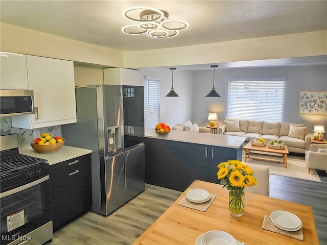 kitchen with light hardwood / wood-style flooring, a textured ceiling, appliances with stainless steel finishes, decorative light fixtures, and white cabinetry