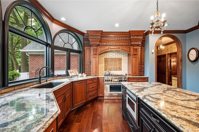 kitchen featuring dark wood-type flooring, ornamental molding, stainless steel appliances, light stone counters, and sink