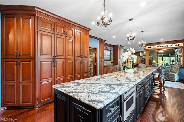 kitchen with an inviting chandelier, a kitchen island, pendant lighting, and dark wood-type flooring