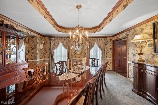 carpeted dining room featuring a raised ceiling, ornamental molding, and an inviting chandelier