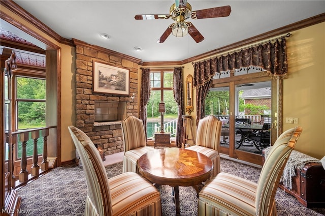 carpeted dining space with a stone fireplace, ornamental molding, and ceiling fan