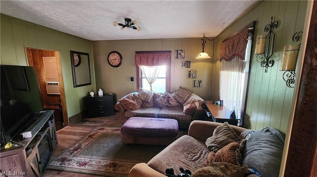 living room featuring dark wood-type flooring, a textured ceiling, and wood walls