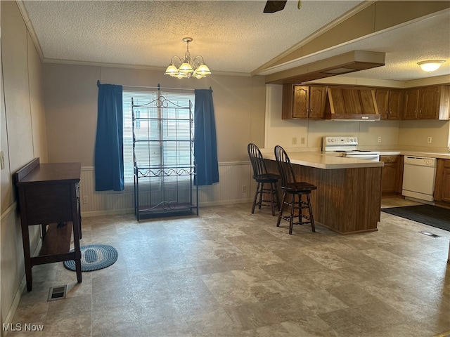 kitchen featuring custom range hood, white appliances, a textured ceiling, decorative light fixtures, and a breakfast bar area