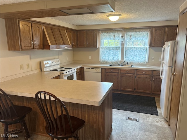 kitchen featuring kitchen peninsula, a kitchen bar, premium range hood, white appliances, and sink