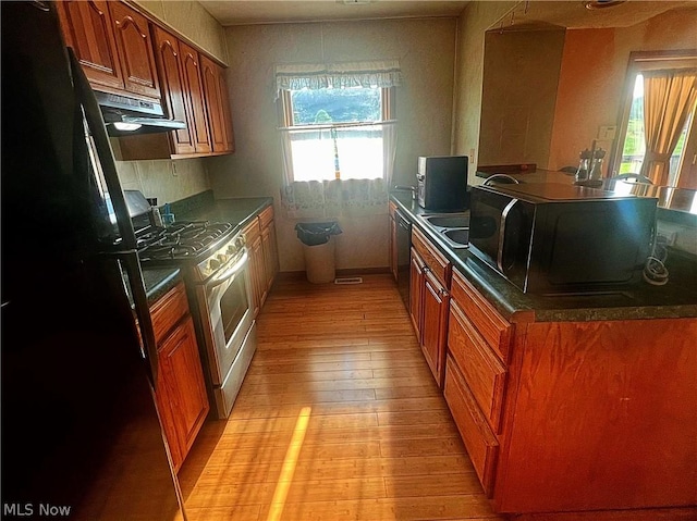 kitchen with dishwasher, black fridge, range hood, light hardwood / wood-style floors, and white range with gas cooktop