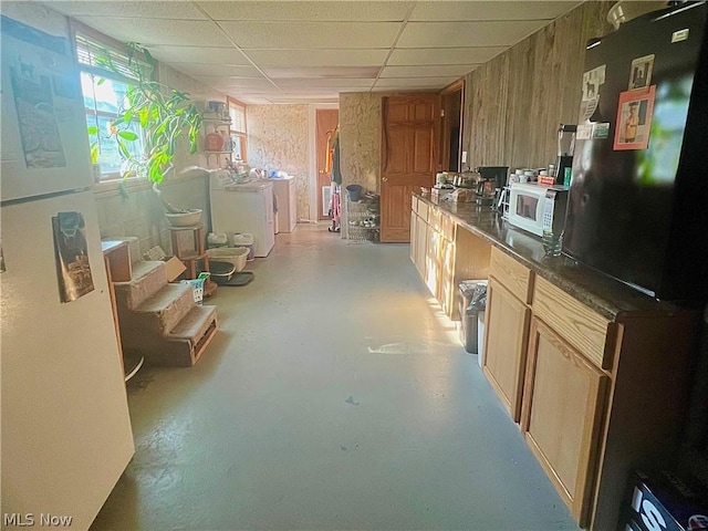 kitchen featuring washer / clothes dryer, wood walls, black refrigerator, and a drop ceiling