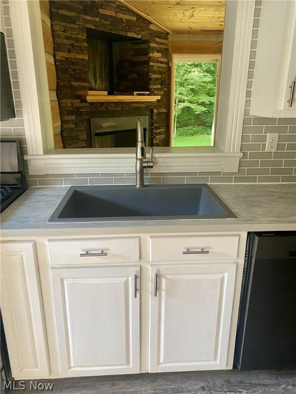 kitchen featuring decorative backsplash, white cabinetry, sink, and black dishwasher