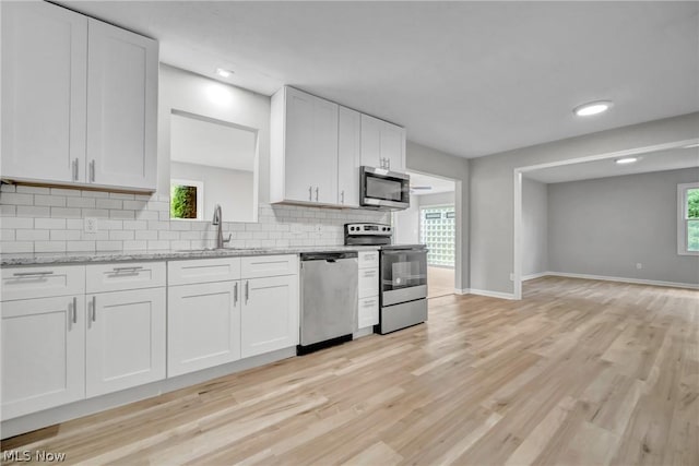 kitchen with white cabinets, appliances with stainless steel finishes, light stone counters, and a wealth of natural light