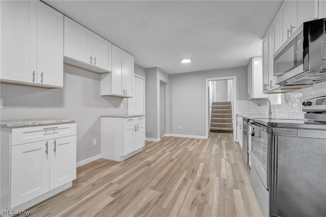 kitchen featuring backsplash, stainless steel appliances, sink, light hardwood / wood-style flooring, and white cabinets