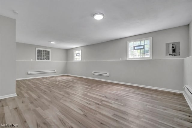 empty room with a healthy amount of sunlight, baseboard heating, electric panel, and light hardwood / wood-style flooring