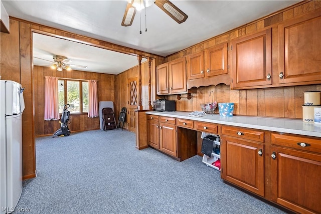 kitchen with ceiling fan, white refrigerator, wood walls, and light colored carpet