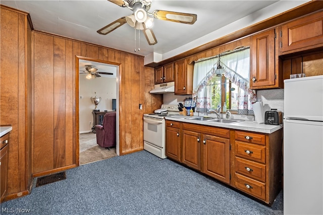 kitchen featuring sink, wooden walls, carpet flooring, white appliances, and ceiling fan