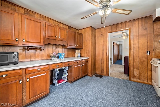 kitchen featuring ceiling fan, wood walls, white range with electric stovetop, and dark colored carpet