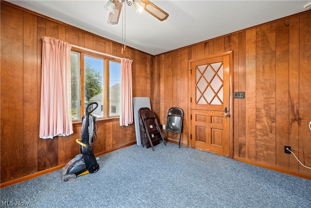 exercise room with ceiling fan, light colored carpet, and wood walls