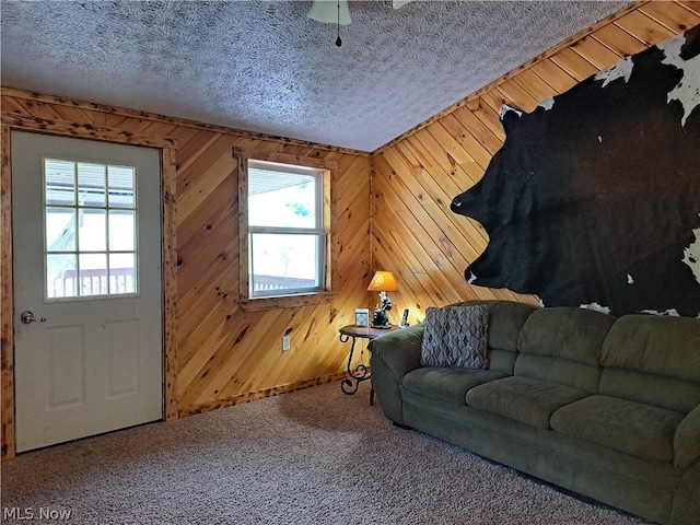 carpeted living room featuring a textured ceiling, a wealth of natural light, and wooden walls